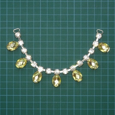 Colar com pedras amarelas em forma de gota e cristais transparentes sobre fundo quadriculado verde