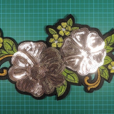 Aplicação de tecido bordada com lantejoulas prateadas e detalhes a verde e castanho