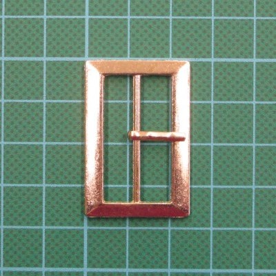 Fivela metálica dourada retangular sobre fundo verde quadriculado