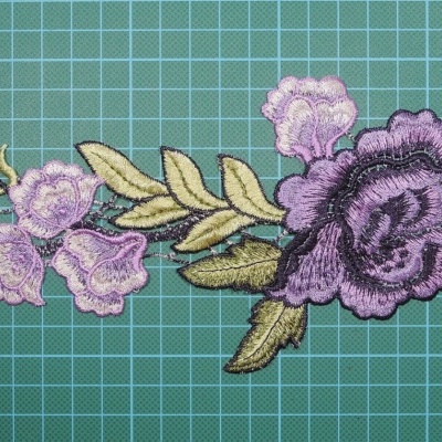 Applique floral bordado lilás e roxo com folhas verdes em fundo verde quadriculado