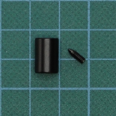 Peça cilíndrica preta e parafuso preto sobre superfície verde com grade azul