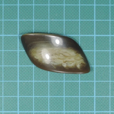 Gema oval assimétrica castanho claro e escuro com padrões internos sobre superfície quadriculada verde