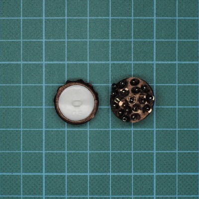 Dois botões redondos, um branco e outro com tachas pretas, sobre superfície verde quadriculada