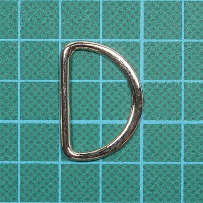 Argola metálica prateada em forma de D sobre fundo verde com grelha azul