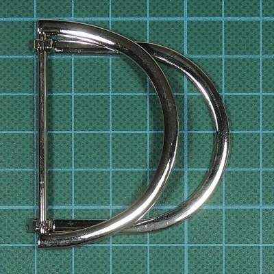 Fivela metálica prateada em formato de D sobre superfície verde quadriculada