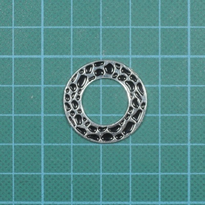 Anel metálico prateado texturizado sobre fundo quadriculado verde