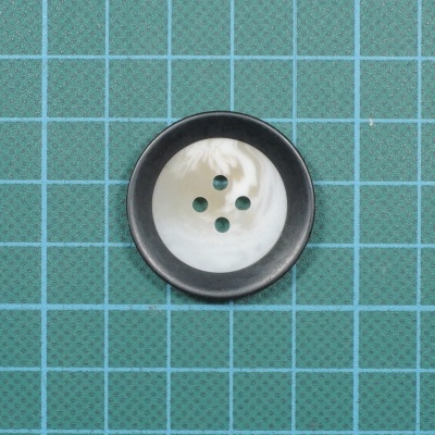 Botão redondo preto e branco marmoreado sobre tecido verde com padrão quadriculado azul