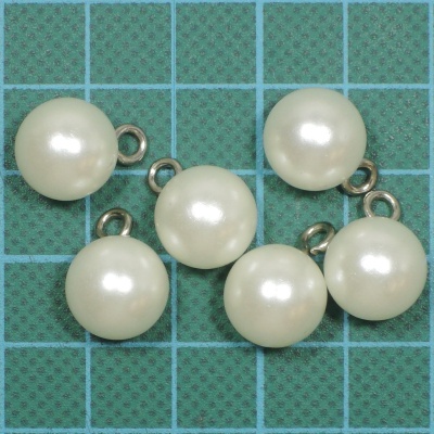 Seis pendentes de pérola branca com argolas metálicas sobre fundo verde quadriculado.