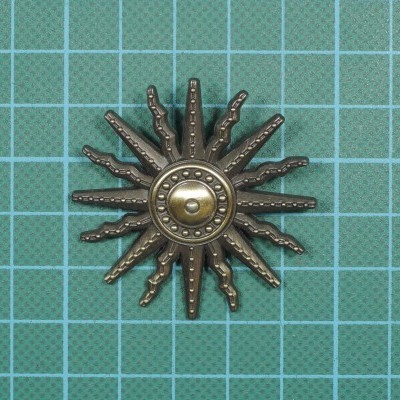 Adorno metálico em forma de sol bronze sobre superfície verde de corte com grade