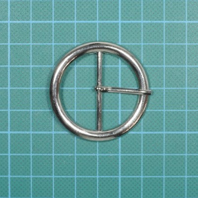 Argola metálica prateada redonda com pino central sobre fundo quadriculado verde