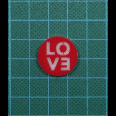 Botão redondo vermelho com letras brancas LOVE sobre fundo quadriculado verde