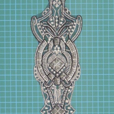 Aplicação bordada intrincada preta e bege sobre fundo azul quadriculado