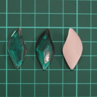 Pedras facetadas verdes e rosa sobre tapete de corte verde com linhas brancas