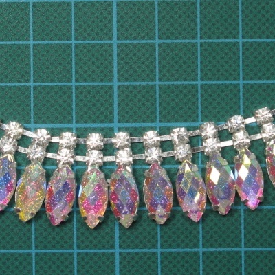 Joia prateada com pendentes de cristais coloridos sobre fundo verde quadriculado.