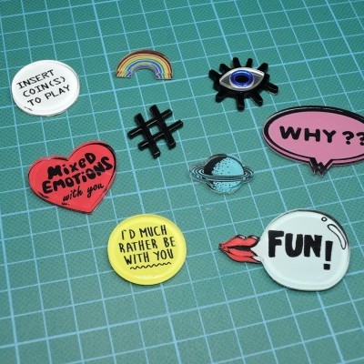 pins decorativos variados com texto e desenhos sobre superfície quadriculada verde