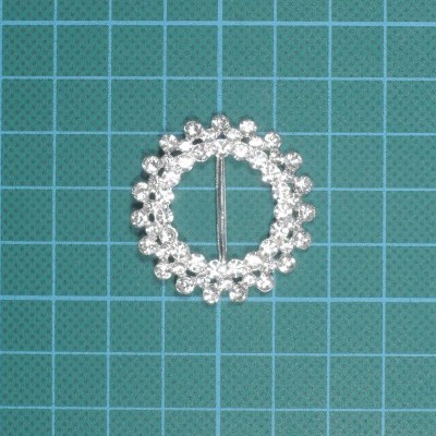 Broche circular com pedras brilhantes sobre tapete verde quadriculado