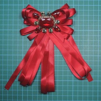 Laço decorativo vermelho em fita de cetim com pedras brilhantes sobre fundo verde quadriculado