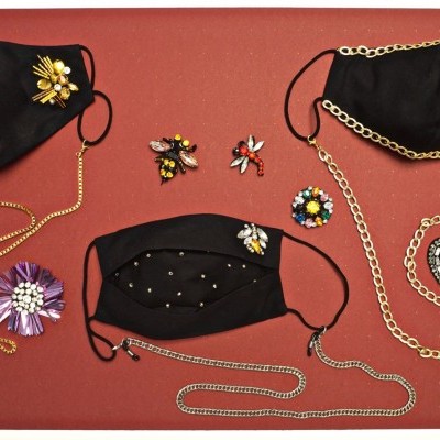 Máscaras pretas decoradas com enfeites e correntes, broches florais e corações sobre fundo vermelho