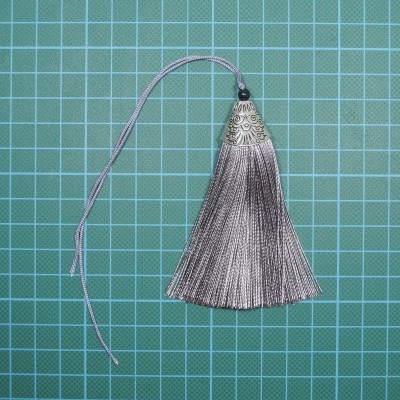 Pendente cinzento com acabamento metálico prateado e padrão gravado sobre tapete de corte verde