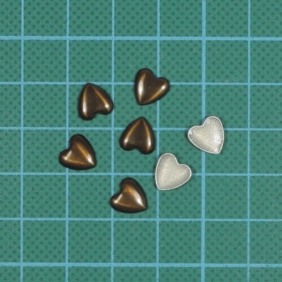 Seis contas em forma de coração douradas e prateadas sobre uma base de corte verde com grade azul clara.