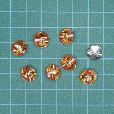 Sete botões redondos em superfície quadriculada verde, seis âmbar translúcidos e um prateado