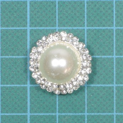 Broche redondo com pérola e strass sobre fundo quadriculado