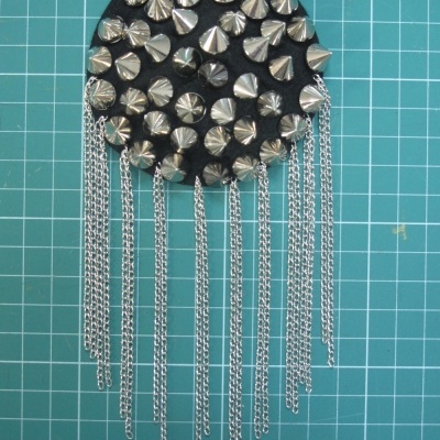 Acessório preto com tachas metálicas e correntes prateadas penduradas