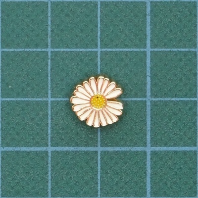 Broche margarida branco e amarelo com contornos dourados sobre fundo verde quadriculado