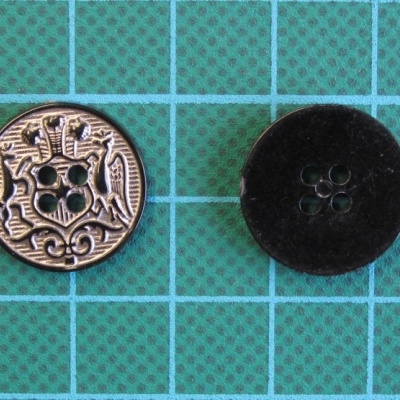 Dois botões redondos, metálico dourado decorado e preto fosco, sobre fundo verde com grelha azul
