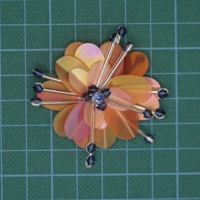 broche flor laranja e roxo em superfície verde com grade