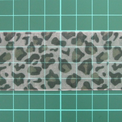 Fita decorativa com padrão de estampa animal em tons cinza e preto sobre superfície verde com grelha branca