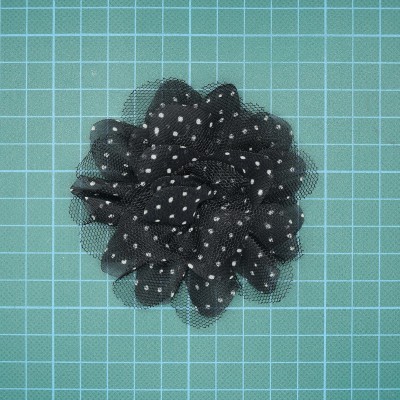 Flor artificial preta com pontos brancos sobre fundo quadriculado