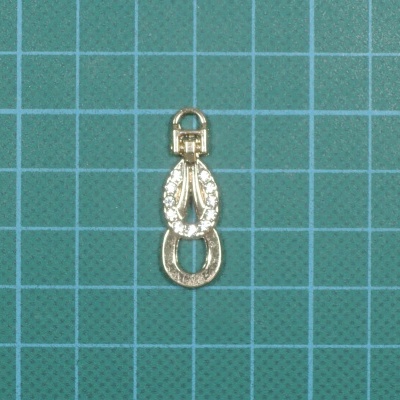 Pendente metálico dourado com pedras brilhantes sobre fundo quadriculado verde