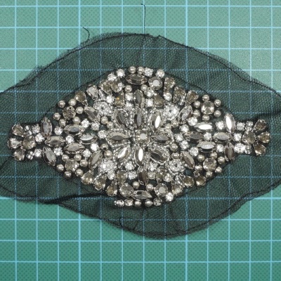 Adereço preto com pedras brilhantes sobre fundo quadriculado verde