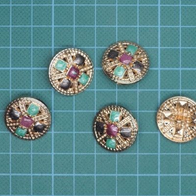 Cinco botões redondos dourados com pedras coloridas em fundo verde quadriculado