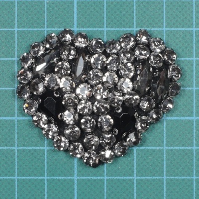 Broche em forma de coração com cristais transparentes e pretos numa superfície azul de grade verde clara