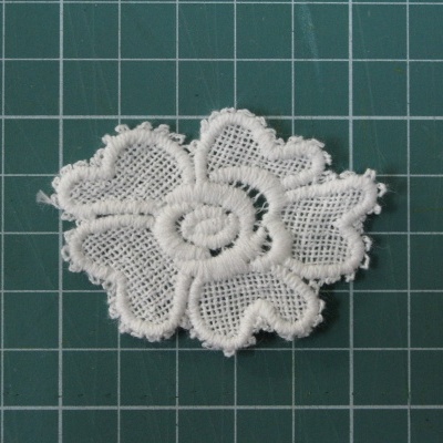 Aplicação em renda branca em forma de flor sobre superfície verde com grade
