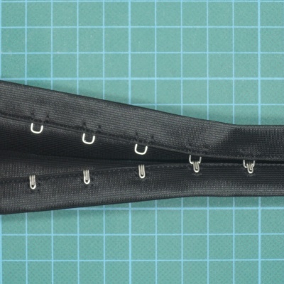 Fecho preto com ganchos de metal em superfície verde com grelha