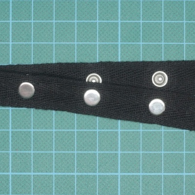 Correia preta com botões de pressão metálicos em fundo de tapete azul quadriculado