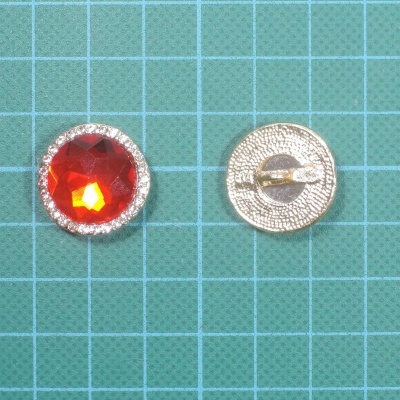Botões metálicos com pedra vermelha e cristais sobre superfície quadriculada verde