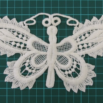 Aplicação de renda branca em forma de borboleta com detalhes rendados sobre superfície verde quadriculada