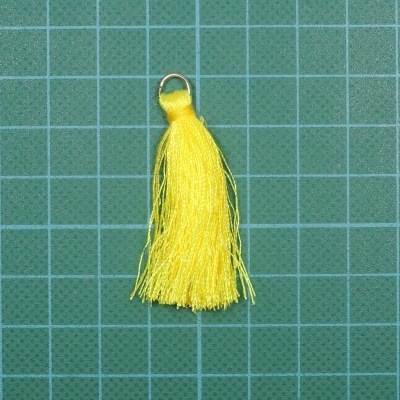 Pendente amarelo de pompom com argola metálica sobre superfície verde quadriculada