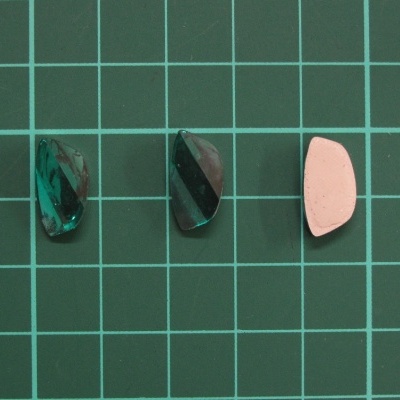 Três pequenas peças geométricas em verde translúcido e rosa claro sobre fundo verde quadriculado