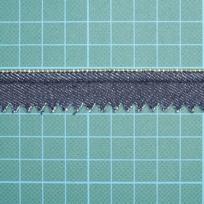 Faixa de tecido preto com acabamento zig-zag sobre tapete de corte verde