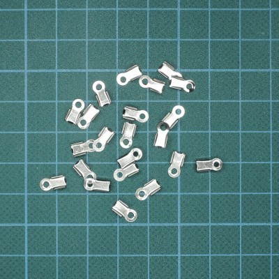 Terminais metálicos prateados para bijuterias sobre base verde quadriculada