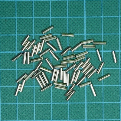 Pequenos cilindros metálicos prateados sobre superfície verde com grelha azul