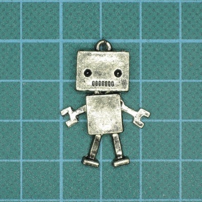 Pendente metálico em forma de robô prateado sobre superfície azul com quadrícula.