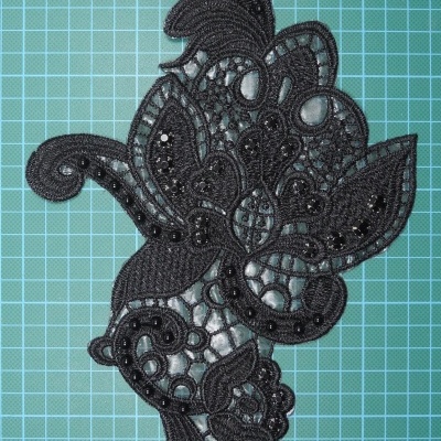 Aplicação de renda preta com pedras pretas, padrão floral, em fundo verde de grade