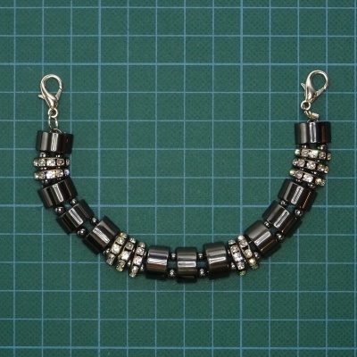 Pulseira com contas pretas cilíndricas e pedras brilhantes sobre fundo quadriculado verde