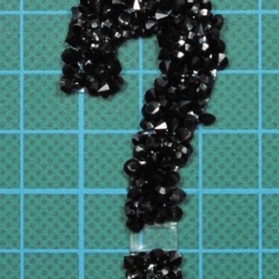 Ponto de interrogação de pedras pretas em fundo quadriculado verde com linhas azuis.